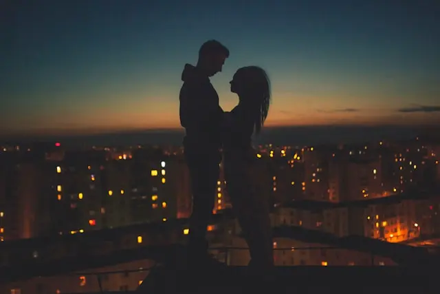 Imagem de um casal abraçados no topo de um predio ao anoitecer representando o conteudo sobre destinos para uma lua de mel